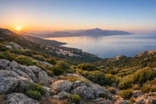Hillside panoramic view over the Gulf of Ajaccio at sunrise, with granite rocks, dense maquis, and tranquil sea, under a clear Mediterranean sky.