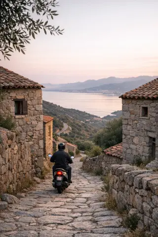 narrow granite street in Villanova at dawn with gulf of Ajaccio in the background and a local on a scooter leaving the village, soft natural light, peaceful Mediterranean atmosphere